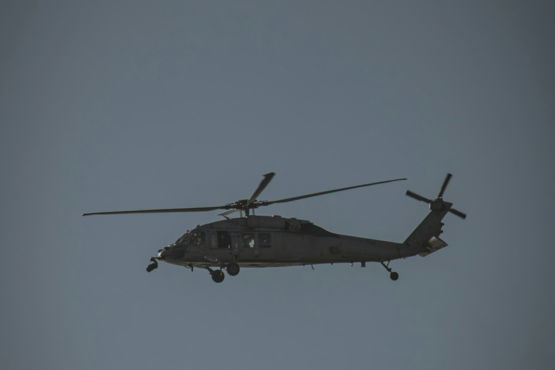 A dark helicopter flies in a clear blue sky.